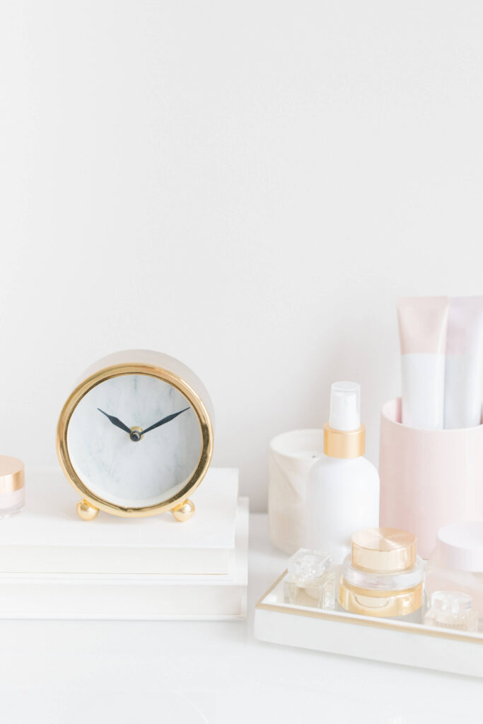 A close-up view of a while desk with a small gold clock resting on a stack of white books.