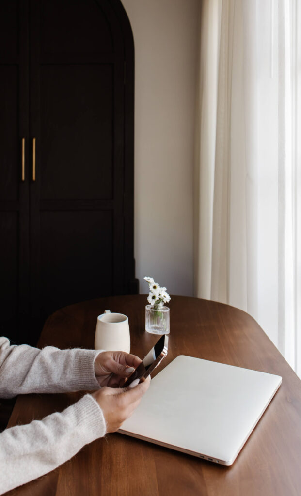 A woman sitting at a desk with a closed laptop, holding her iphone.